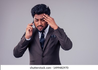 Professional Stress Problem At Work:portrait Of Depressed Business Upset Indian Man Speaking By Mobile Phone About Nervous Deal In Studio White Background.