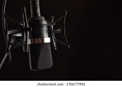 Professional Studio Condenser Microphone in Shock Mount  with Pop Filter on Left with Space for Type, Isolated on Black Background