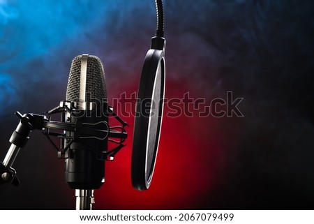 Professional studio microphone with pop filter on red-blue smoke background. Nightclub, singing, spoken word, television, radio, recording studio, instrumental music.