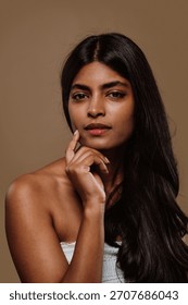 Professional studio portrait capturing young indian woman with long dark hair expressing genuine emotions while posing against neutral brown background