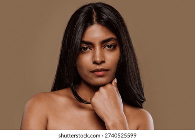 Professional studio portrait capturing young indian woman with long dark hair expressing genuine emotions while posing against neutral brown background
