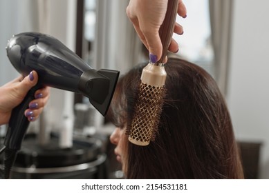 Professional stylist making hairstyle using hair dryer and brush