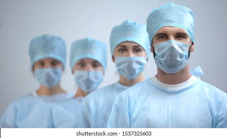 Professional surgeon team in mask and uniform looking at camera, hospital work