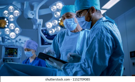 Professional Surgeons and Assistants Talk and Use Digital Tablet Computer while Standing in the Modern Hospital Operating Room. - Powered by Shutterstock