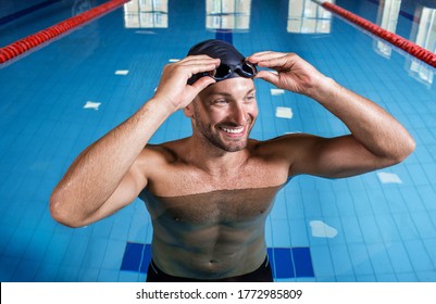 A professional swimmer man adjusting his swimming goggles, smiles and looking away. Swimming pool coach - Powered by Shutterstock