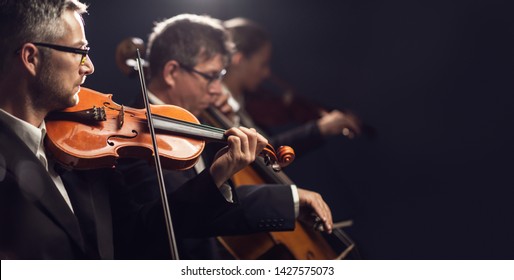 Professional Symphonic Orchestra Performing On Stage And Playing A Classical Music Concert, Violinist Playing In The Foreground, Arts And Entertainment Concept