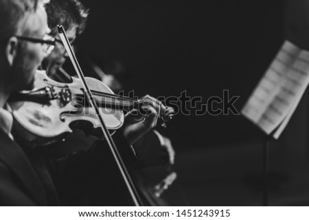 Professional symphonic orchestra performing on stage and playing a classical music concert, violinist playing in the foreground, arts and entertainment concept