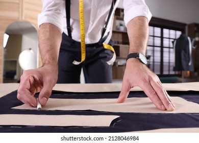 Professional tailor marking sewing pattern on fabric with chalk at table in workshop, closeup