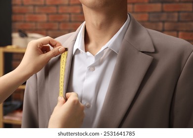 Professional tailor measuring jacket lapel on client in atelier, closeup - Powered by Shutterstock