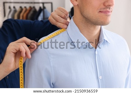 Professional tailor measuring shoulder seam length on client's shirt in atelier, closeup