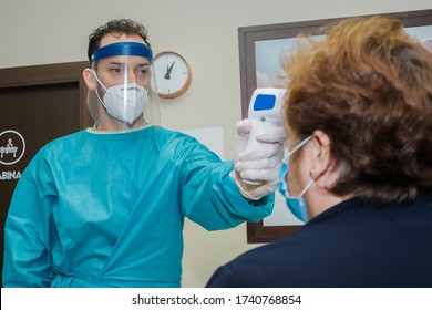 A Professional Taking The Patient's Temperature Before The Physiotherapy Session. The Patient And The Professional Have Masks And Protective Gloves. Hygiene Measures To Avoid The Covid 19.