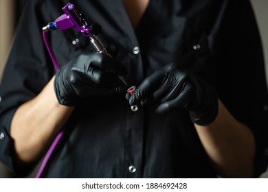 A Professional Tattoo Artist In A Black Robe And Black Gloves Holds A Tattoo Machine In His Arm.