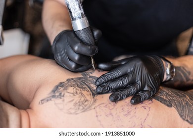 プロの刺青師が刺青機械の針を使って、黒いインクを肌に導入します。 体に刺青を入れる。 スタジオで白黒のタトゥーを入れるプロの入れ墨師。