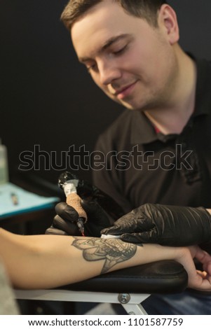 Professional tattoo artist making beautiful tattoo on young woman hand. Man tattooist drawing floristic picture on female arm with special machine, copy space