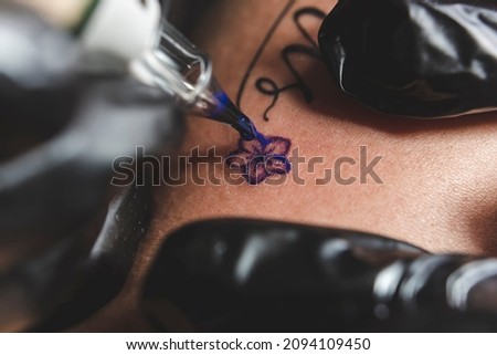 A professional tattoo artist uses a rotary tattoo machine to shade a small flower. Using a round liner and purple ink.