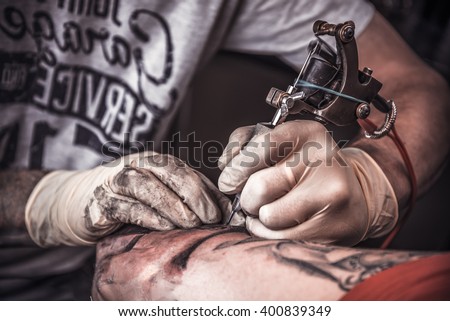 Professional tattooer burning the tatoo with gloves on by special tool closeup.