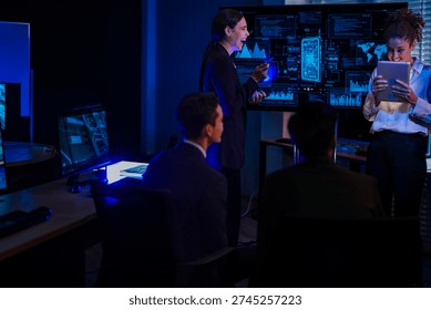 Professional IT team analyzing global network security dashboard in modern control center. Female manager leading cyber technology project discussion in dark night office.