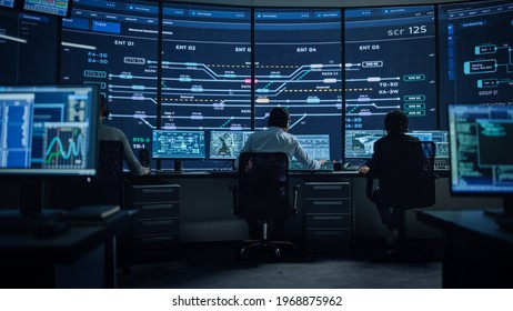 Professional IT Technical Support Specialists And Software Programmer Working On Computers In Monitoring Control Room With Digital Screens With Server Data, Blockchain Network And Surveillance Maps.