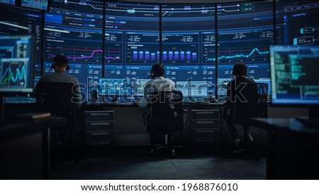 Professional IT Technical Support Specialists and Software Programmer Working on Computers in Monitoring Control Room with Digital Screens with Server Data, Blockchain Network and Surveillance Maps.