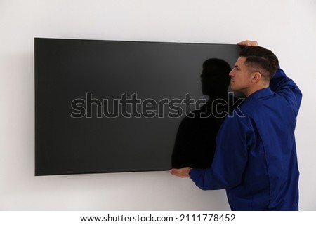 Professional technician installing modern flat screen TV on wall indoors