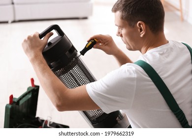 Professional Technician Repairing Electric Patio Heater With Screwdriver Indoors