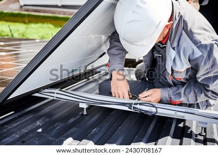 Professional technician securing cables by cable tie. Male worker using special equipment to secure solar cell well. Close up view of man specialist installing solar panel.