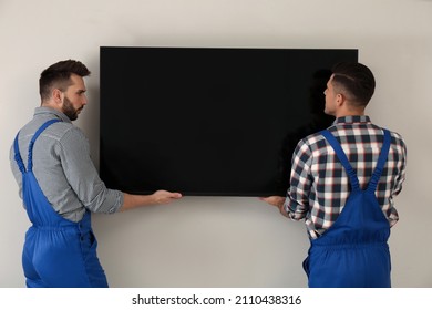 Professional Technicians Installing Modern Flat Screen TV On Wall Indoors