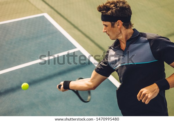 Professional\
tennis player hitting forehand on hard court. Young man in\
sportswear playing tennis on tennis\
court.