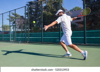 Professional tennis player playing a game of tennis on a court. He is about to hit the ball with the racket. The ball is suspended in the air. 
