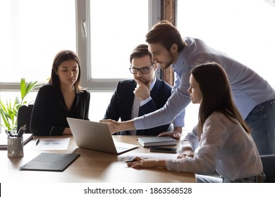 Professional training. Capable millennial male mentor explaining group of interns business project details on laptop screen, skilled young man team leader allocating task between diverse staff members