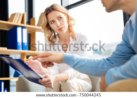 Professional treatment. Nice smart pleasant man pointing at the notes and asking a question to his therapist while having a psychological session