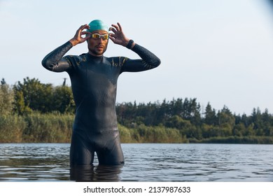 Professional Triathlete Before Swimming In River's Open Water. Man Wearing Swim Equipment Practicing Triathlon On The Beach In Summer's Day. Concept Of Healthy Lifestyle, Sport,