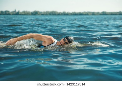 Professional Triathlete Swimming In River's Open Water. Man Wearing Swim Equipment Practicing Triathlon On The Beach In Summer's Day. Concept Of Healthy Lifestyle, Sport, Action, Motion And Movement.