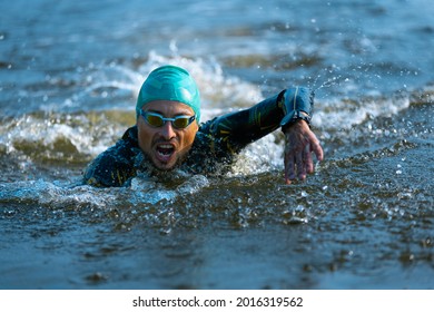 Professional triathlete swimming in river's open water. Man wearing swim equipment practicing triathlon on the beach in summer's day. Concept of healthy lifestyle, sport, action, motion and movement. - Powered by Shutterstock