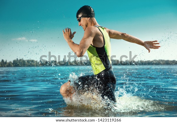 Professional triathlete swimming in river\'s\
open water. Man wearing swim equipment practicing triathlon on the\
beach in summer\'s day. Concept of healthy lifestyle, sport, action,\
motion and\
movement.