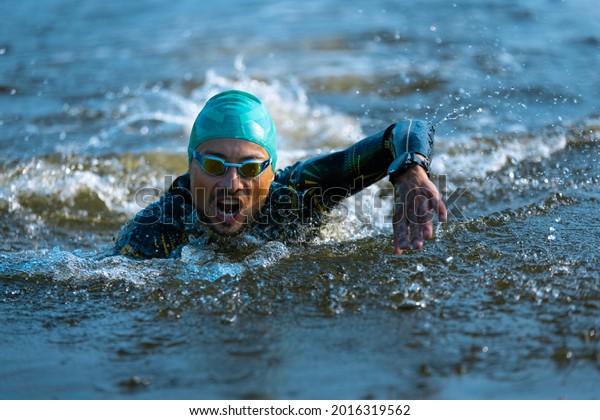Professional triathlete swimming in river\'s\
open water. Man wearing swim equipment practicing triathlon on the\
beach in summer\'s day. Concept of healthy lifestyle, sport, action,\
motion and\
movement.