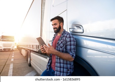 Professional truck driver checking his route on tablet computer and standing by long vehicle. Transportation service.