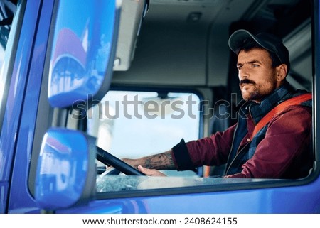 Professional truck driver driving in reverse while looking in side view mirror.