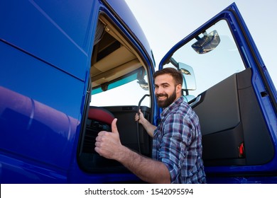 Professional truck driver entering his truck long vehicle and holding thumbs up. Loving his job. Transportation services.