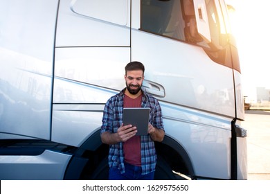 Professional Truck Driver. Young Bearded Trucker Checking His Route On Tablet Computer With Dispatcher And Standing By Long Vehicle. Transportation Service.