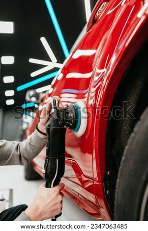Professional vehicle polishing and detailing service in a modern car workshop. Brightly lit workspace with large led lights. High quality car valeting concept.