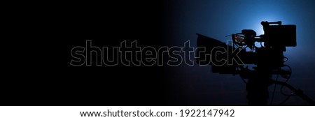 Professional video camera silhouette in the dark with blue light, movie production or television background banner with copy space