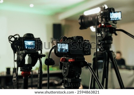 A professional video production setup featuring multiple cameras on tripods, capturing footage in a studio environment with lighting and cables, showcasing high-quality filmmaking equipment