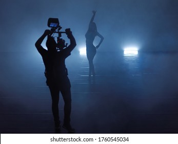 Professional videographer with gimball video slr recording video of female athletic dancer  while performing modern style ballet making acrobatic elements in a dark environment