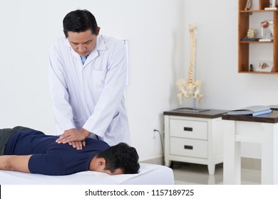 Professional Vietnamese chiropractor doing pushing motion to adjust spine of male patient - Powered by Shutterstock