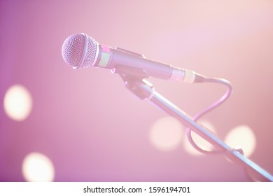 Professional Vocal Microphone On Stage In Music Hall.Retro Style Mic On Stand In Close Up.Pink Vibrant Lights On Scene.Sing A Song Using Pro Audio Equipment