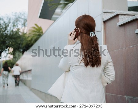 Professional walking on a sidewalk while talking on the phone near a modern building, concept of work on the move, active schedule and executive communication