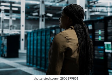 IT professional walking in server facility with mainframes supporting business needs. Data center staff member doing checkup, supporting electronics work at optimum performance for smooth operations.