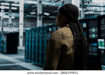 IT professional walking in server facility with mainframes supporting business needs. Data center staff member doing checkup, supporting electronics work at optimum performance for smooth operations.