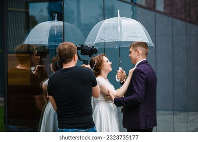 Professional wedding videographer shoots a movie with the newlyweds under an umbrella next to a glass wall - Powered by Shutterstock